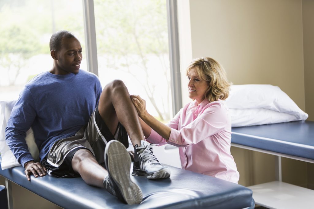 Physical therapist helping patient on exam table with knee stretches