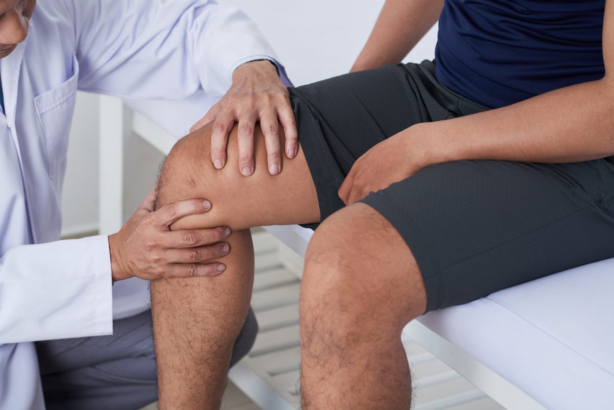 Knee specialist examines knee of patient sitting on exam table