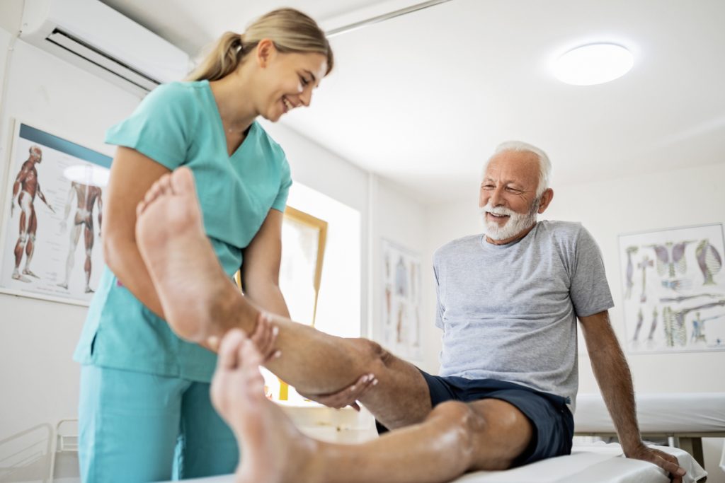 Young physical therapist helping patient with leg exercise