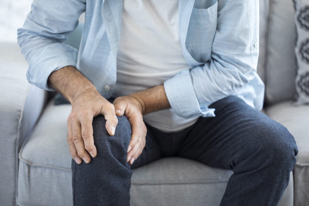 Old man suffering from knee pain sitting on couch