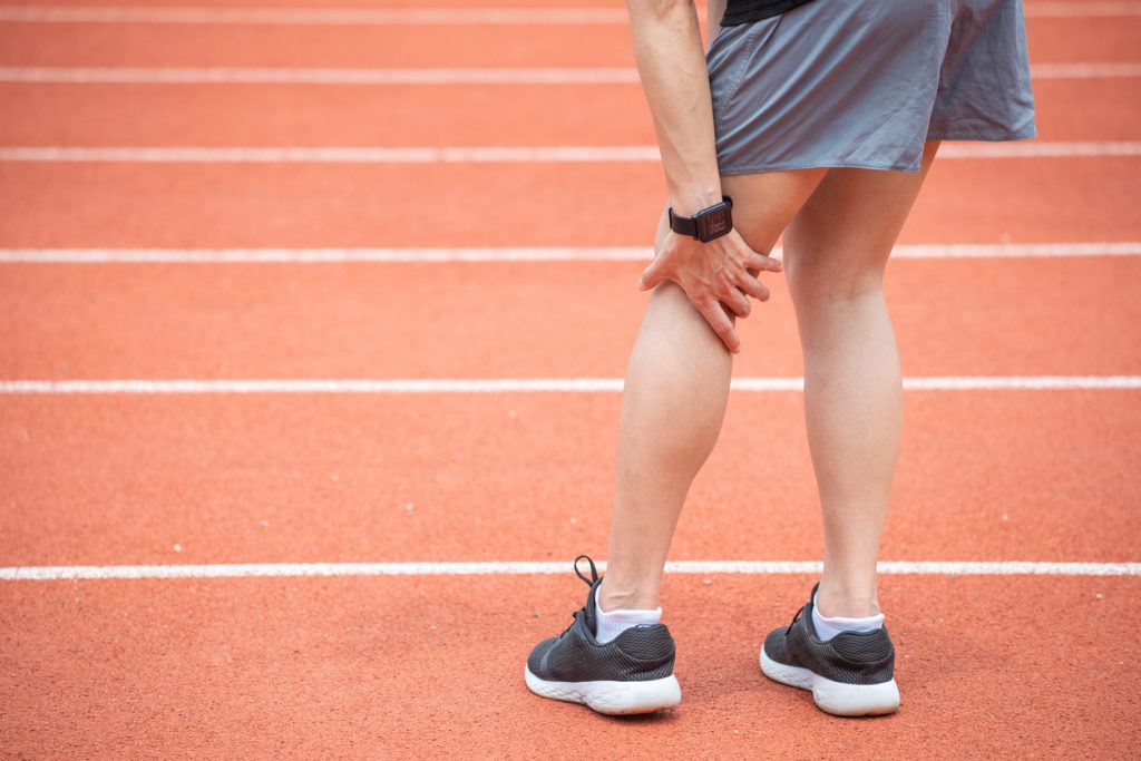 Person on running track bending over and holding back of knee in pain